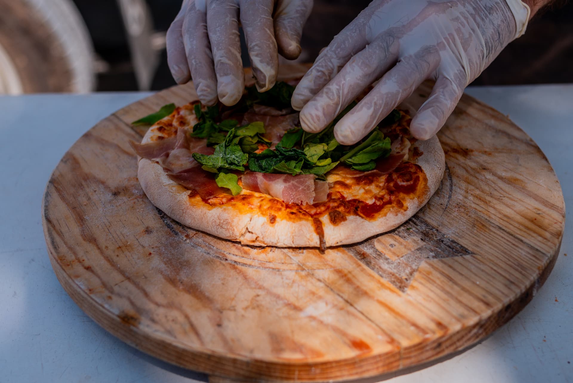 Hands finishing an Italiana pizza with prosciutto and arugula on a wooden board